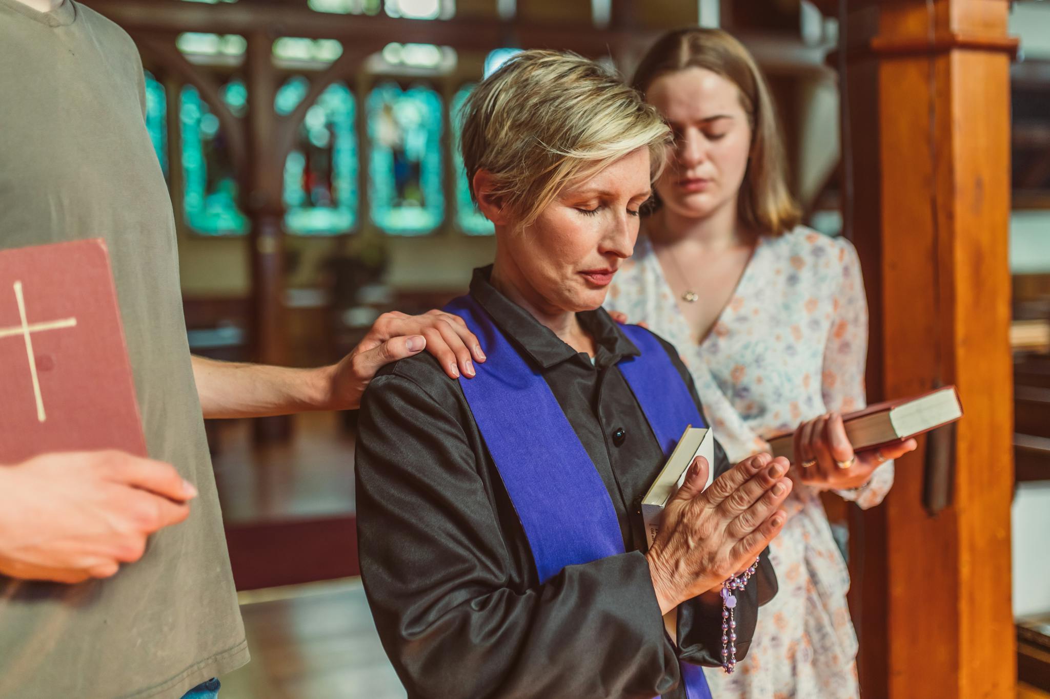 A group of women in prayer with a priest inside a church, embracing faith together.